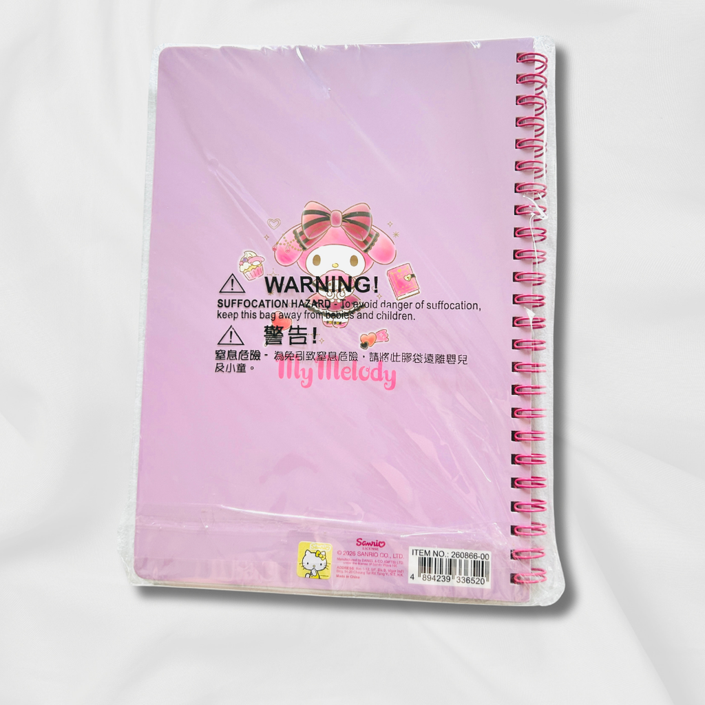 A pink spiral notebook in clear plastic packaging, featuring a cartoon character illustration and warning labels on the front cover.