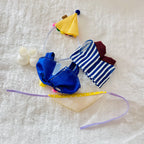 A back view of a labubu doll clothing set. The set includes a blue satin overall, a blue-and-white striped top, a yellow party hat, a bib and a pairs of boots.