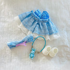 A back view of doll outfit set ncluding a light blue and white gingham ruffled dress with white lace trim, a matching headband with a pink bow, a blue keychain with a bunny charm.