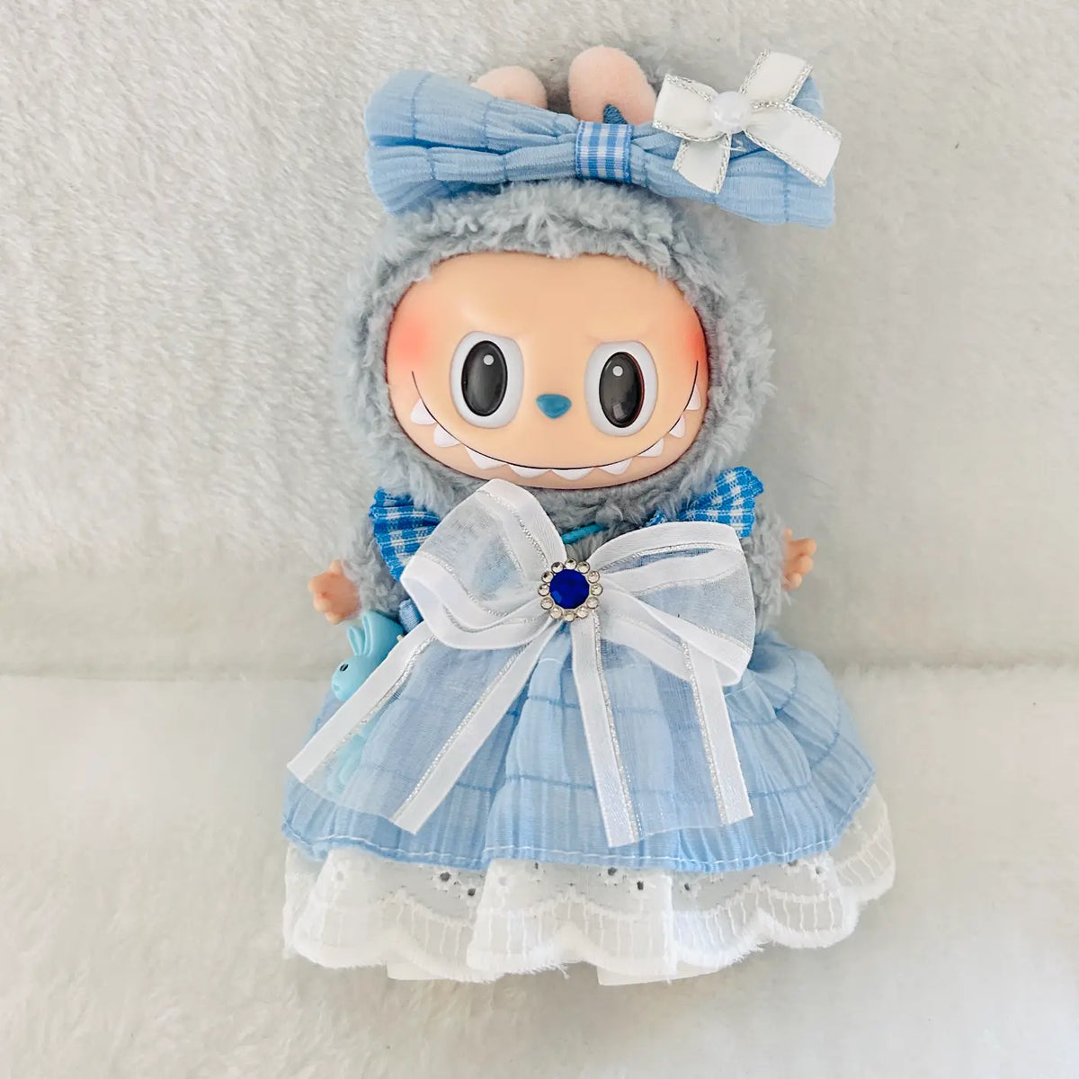 A plush doll wearing a light blue dress with white lace trim and a large white bow at the waist.  