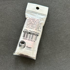 A small sealed white plastic package containing a single round coin or medallion, photographed on a dark textured fabric background. The package has printed text, a barcode, and a visible Sanrio logo near the bottom.