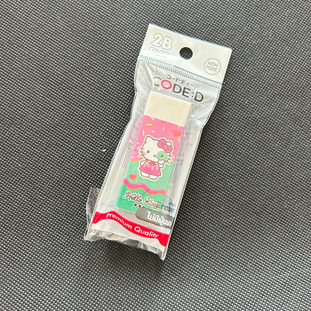 A packaged Hello Kitty eraser on a textured gray fabric background. The eraser is sealed in a clear plastic bag with a printed header card that reads 'CODE:D' and '28 TOYS', featuring a pink and green Hello Kitty design.