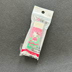 A packaged Hello Kitty eraser on a textured gray fabric background. The eraser is sealed in a clear plastic bag with a printed header card that reads 'CODE:D' and '28 TOYS', featuring a pink and green Hello Kitty design.