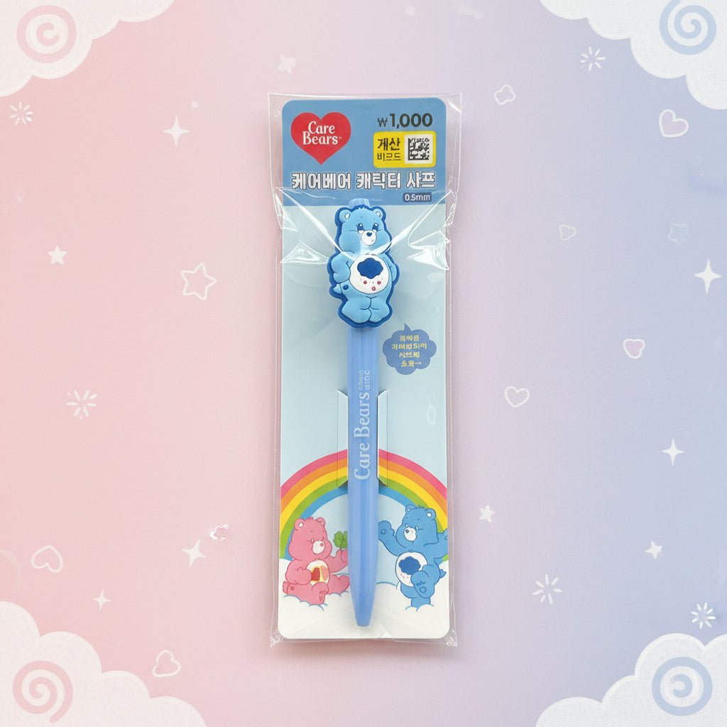 A Care Bears themed blue pen in its original plastic packaging, displayed against a pastel pink and purple background decorated with white clouds and stars.