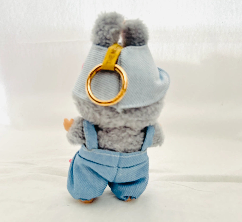 A small gray plush toy or character accessory shown from the back, wearing a light blue denim-style hat and matching overalls, with a gold ring attached near the hat.
