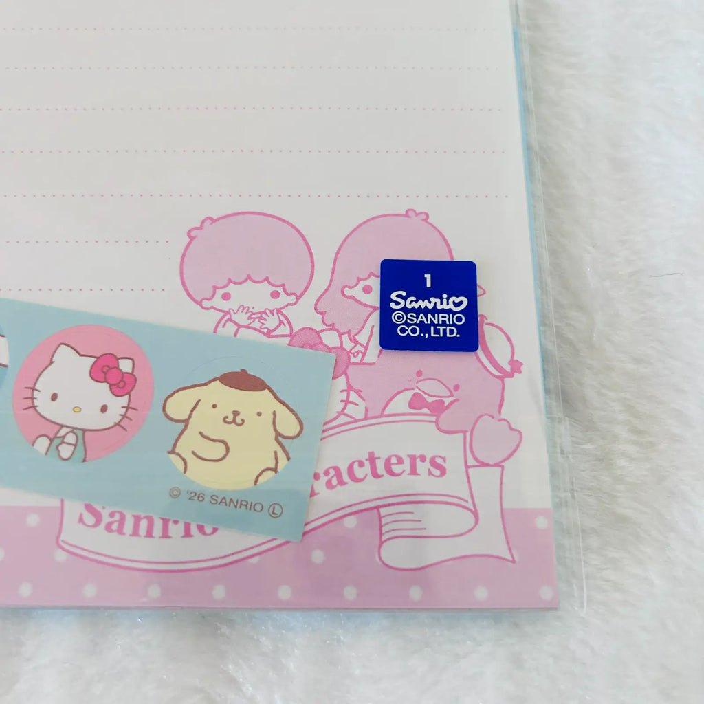 A Sanrio-themed stationery item, likely a notepad or memo pad, featuring pink cartoon characters and a blue Sanrio logo sticker. A small card with Hello Kitty and Pompompurin is placed in front on a white textured fabric background.
