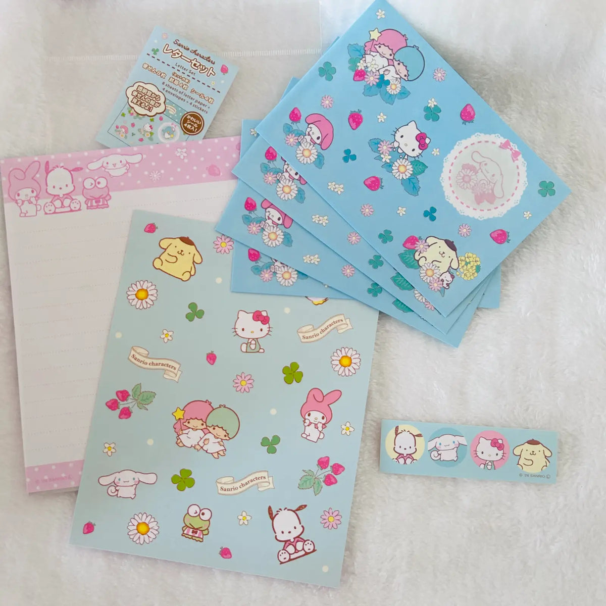 A set of Sanrio Hello Kitty and duo-style character letter set  arranged on a white textured fabric background, including a envelopes,  letter papers and stickers.