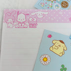 Sanrio character notepad with pink and white sections featuring My Melody, Pichi Pichi, and Cinnamoroll, alongside a light blue sticker sheet with Pompompurin.