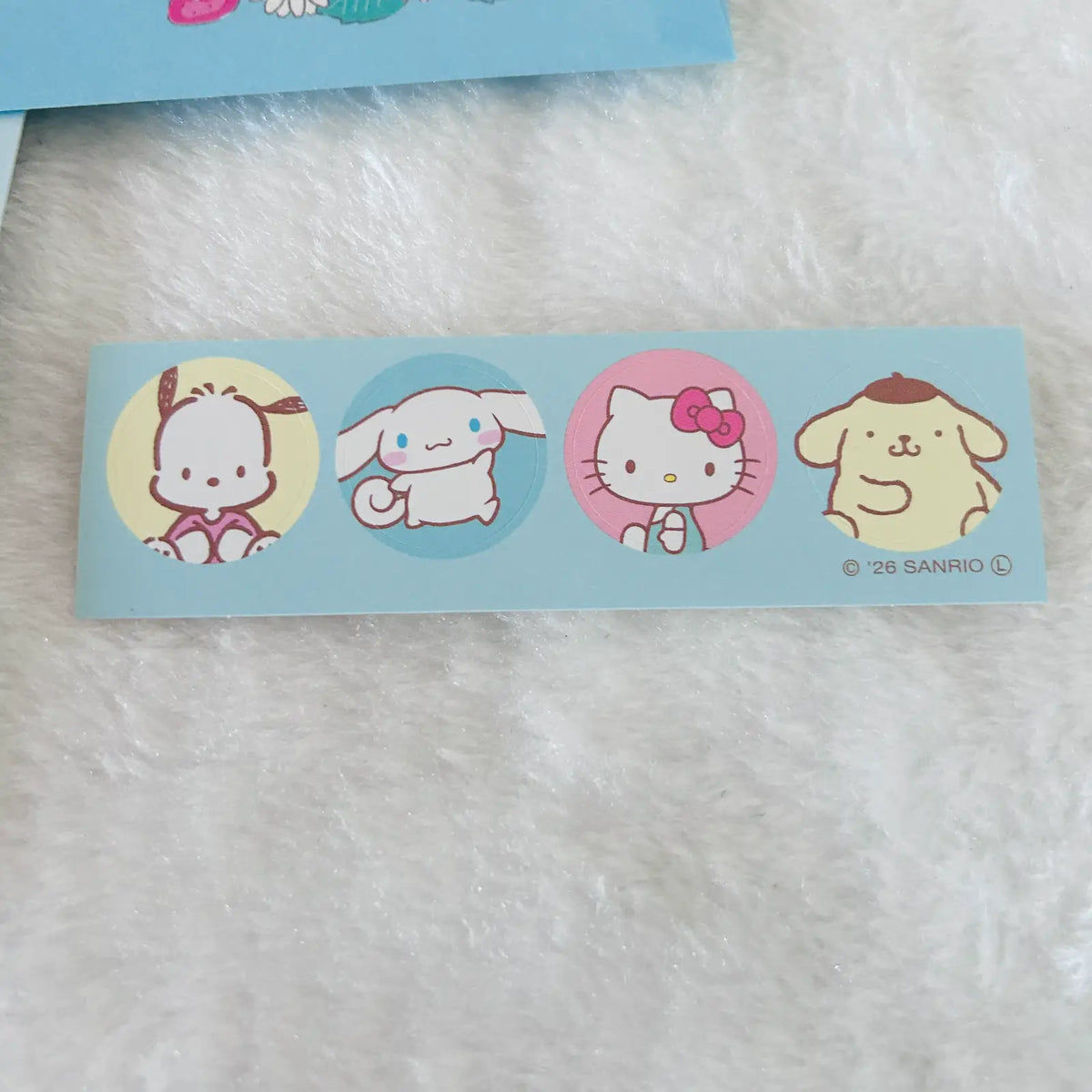 A light blue sticker strip featuring Sanrio characters including Cinnamoroll, Hello Kitty, and Pompompurin on a white faux fur background.
