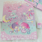 A pastel pink and lavender Little Twin Stars notebook or folder featuring cartoon characters, stars, and whimsical illustrations, placed on a white textured surface with other stationery items partially visible.