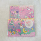 A packaged Little Twin Stars stationery set displayed on a soft white textured surface. The set includes a pink unicorn-themed sheet and a pastel rainbow-themed sheet with character illustrations and a clear window.
