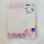 A Sanrio Little Twin Stars lined notepad sheet in a clear plastic sleeve, displayed on a white textured fabric background. The notepad features pink and pastel character illustrations, including Twin Stars and a pink bunny, with a blue Sanrio logo sticker in the bottom right corner.