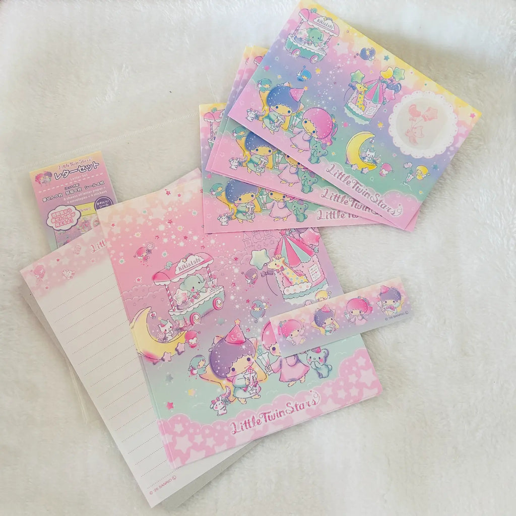 A set of pastel pink and purple Little Twin Stars stationery items, including a lined notepad, a washi tape roll, and several small cards or stickers, arranged on a soft white textured fabric background.