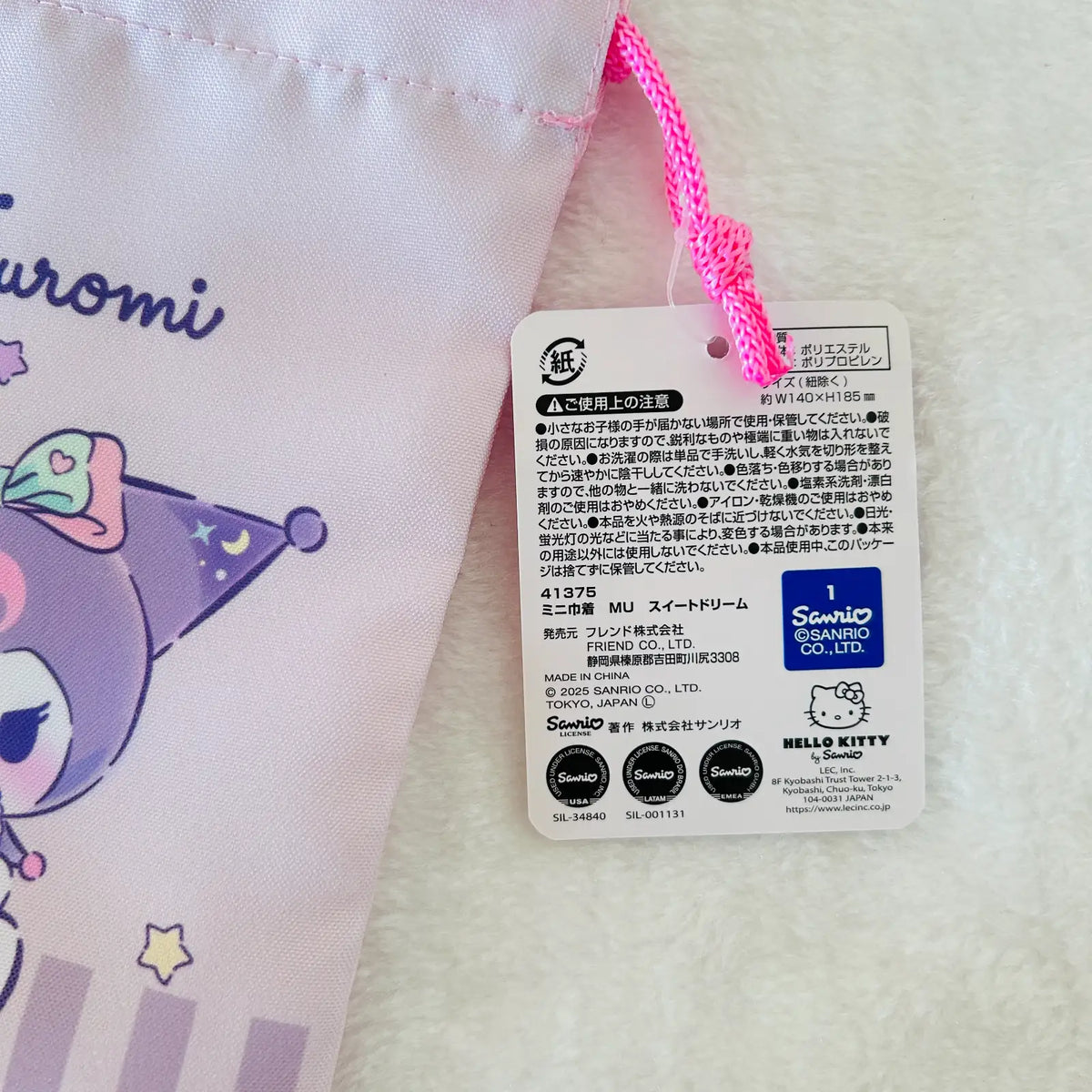 Close-up of a Sanrio Hello Kitty and Kuromi product tag attached to a light pink fabric item with a bright pink drawstring, on a white textured background.