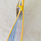 A close-up of a clear plastic zipper pouch with a bright yellow zipper and yellow pull tab, shown against a light beige textured background.
