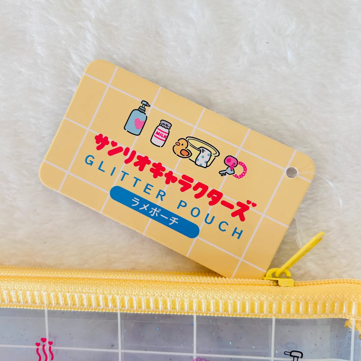 A yellow glitter character pouch with a matching yellow zipper and a printed product tag reading 'GLITTER POUCH' and Japanese text, placed on a white furry surface.