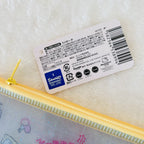 A close-up of a Sanrio Hello Kitty zippered pouch with a yellow zipper and pastel glittery interior, resting on a white textured surface. The product's white hangtag is visible, showing Sanrio branding and a barcode.