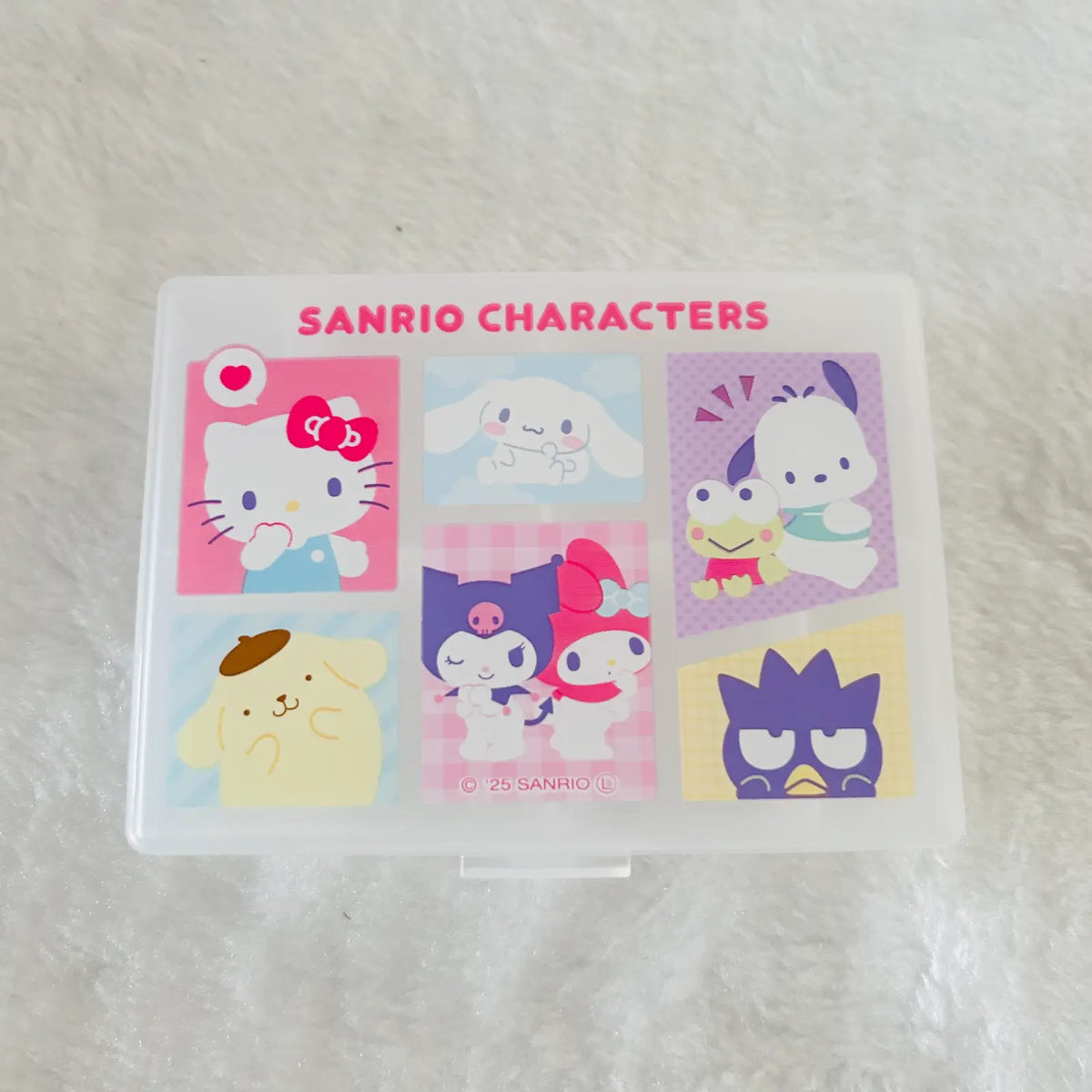 A clear plastic storage box with a printed Sanrio Characters design on the lid, featuring six cartoon panels and the text 'SANRIO CHARACTERS' in pink, placed on a white textured surface.