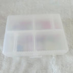 A translucent white plastic organizer box with four compartments, shown on a white textured fabric background.