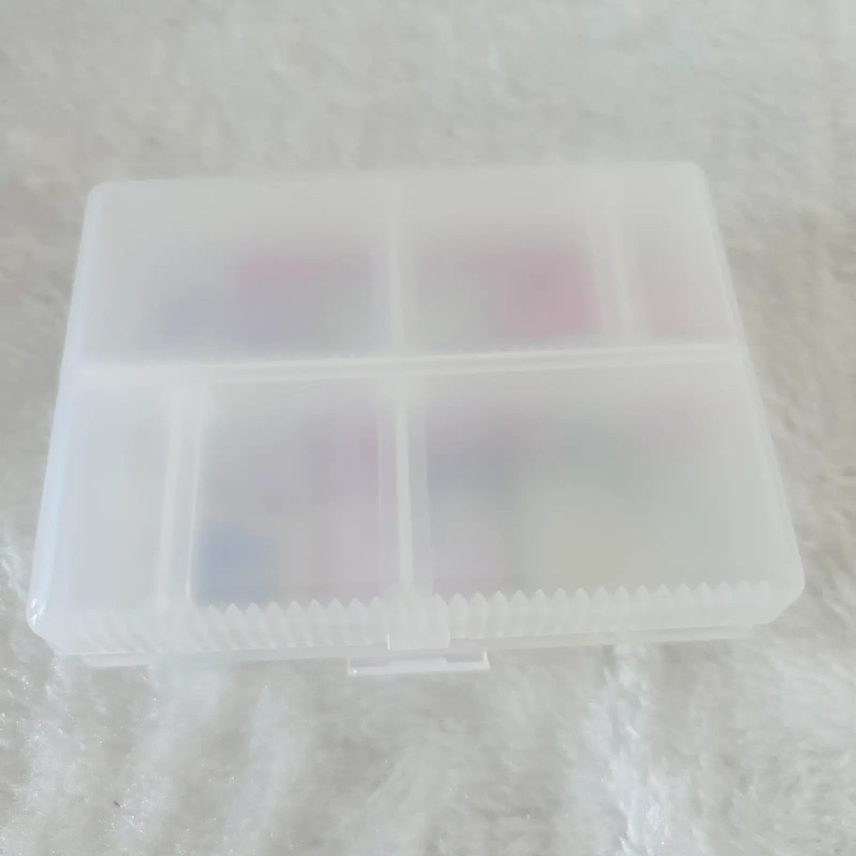 A translucent white plastic organizer box with four compartments, shown on a white textured fabric background.