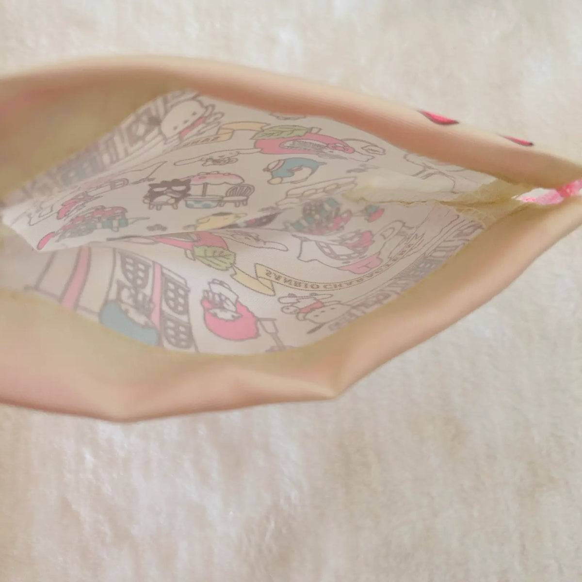 A close-up of a beige fabric pouch or bag with a colorful cartoon character print lining the interior, photographed on a soft white textured background.
