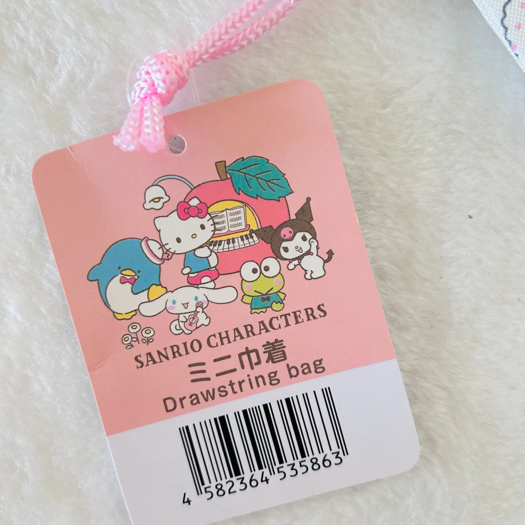 A pink Sanrio Characters drawstring bag tag with cartoon character illustrations and a barcode, photographed on a soft white textured surface.