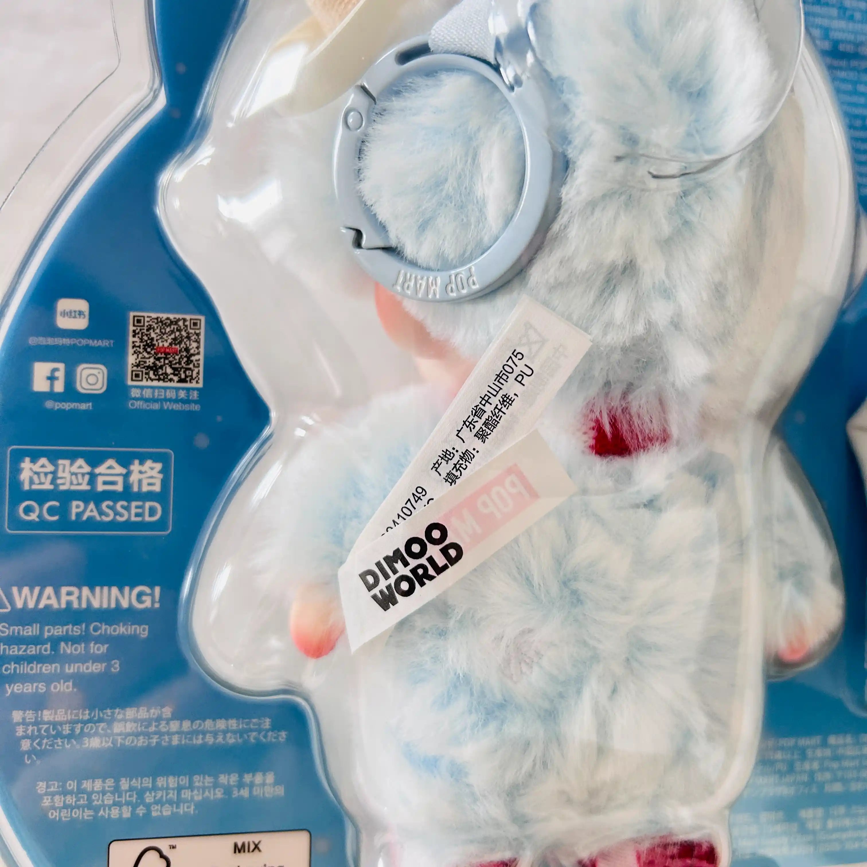 A back view of a  Dimoo Snowman plush toy  in clear blister packaging, shows QR code and  'DINOO WORLD' tag.