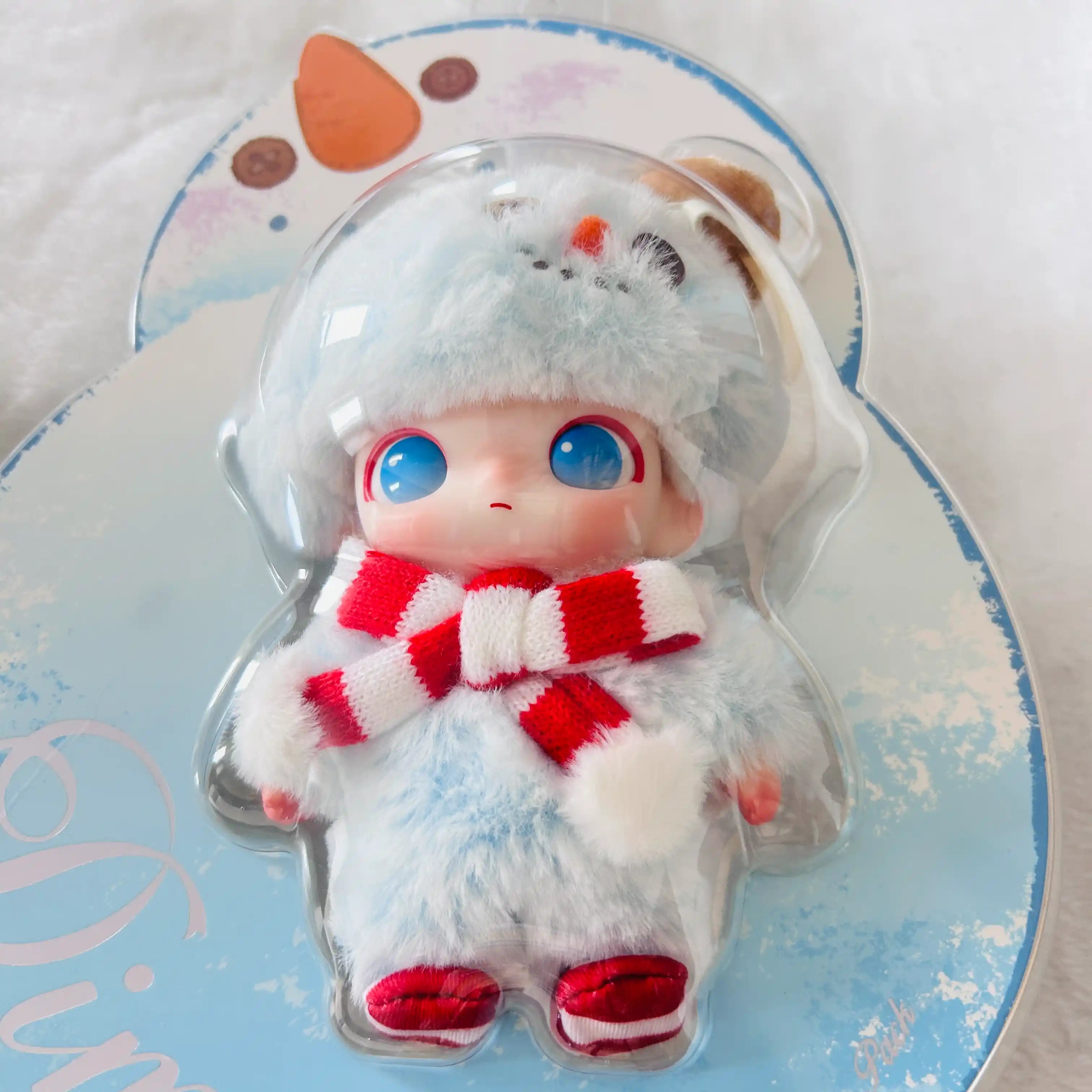A small Dimoo Snowman plush doll dressed in a fluffy light blue winter outfit with a red-and-white striped scarf and red shoes.
