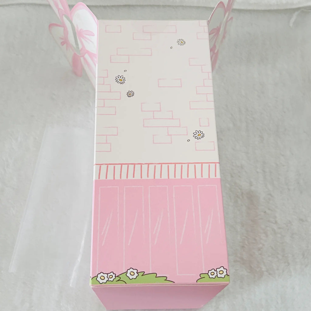 A pink and white decorative gift box with butterfly and flower illustrations, photographed on a soft white textured surface.