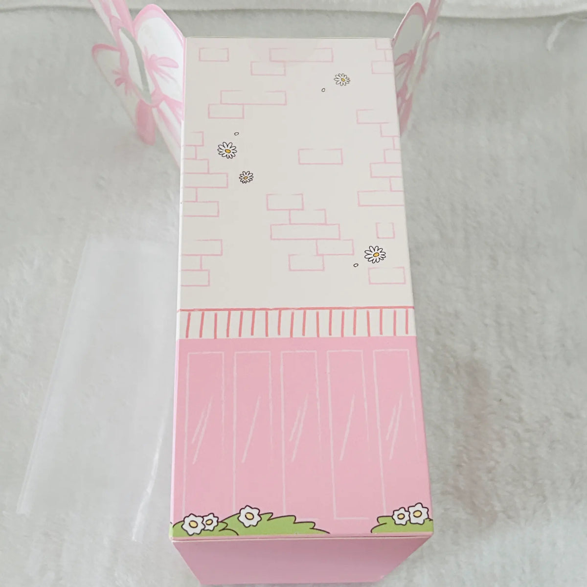 A pink and white decorative gift box with butterfly and flower illustrations, photographed on a soft white textured surface.