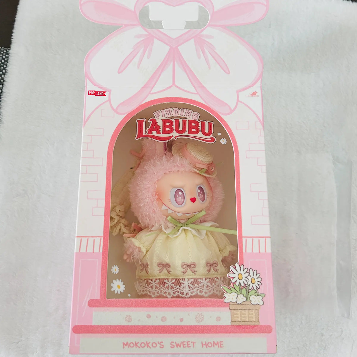 A pink and white LALUBU 'Mokoko's Sweet Home' collectible doll figure in its original retail packaging, displayed on a white textured fabric background.