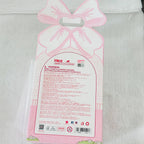 Pink and white decorative gift bag packaging with a bow-shaped handle and a large warning label on the front, photographed on a white textured fabric background.