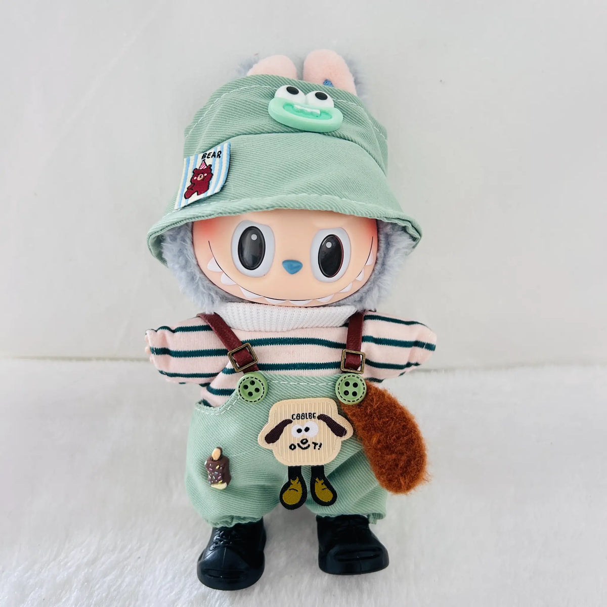 A cute plush doll with a light green bunny hat, striped shirt, green overalls, and black shoes, standing against a white background.