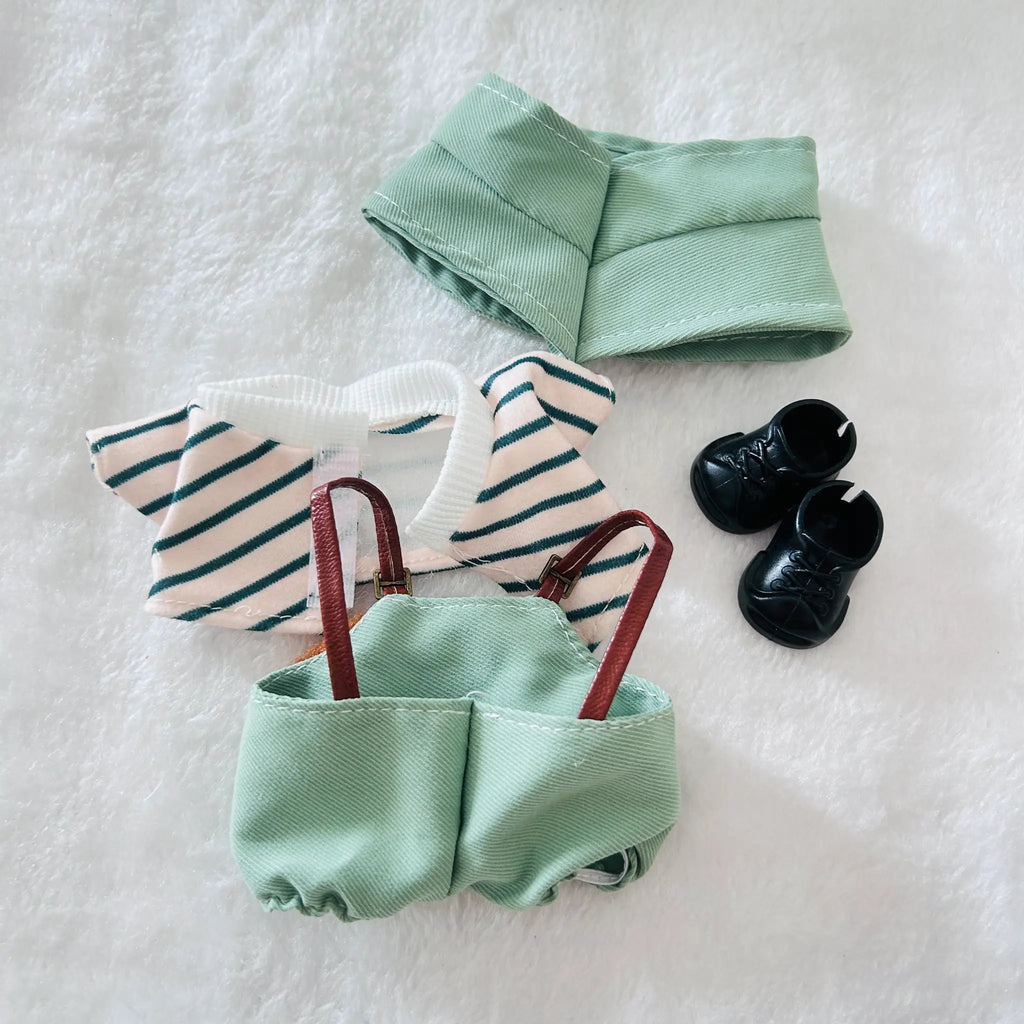 A doll outfit set laid flat on a white textured background, including a mint green skirt, a top with dark green stripes, a matching mint green overalls.