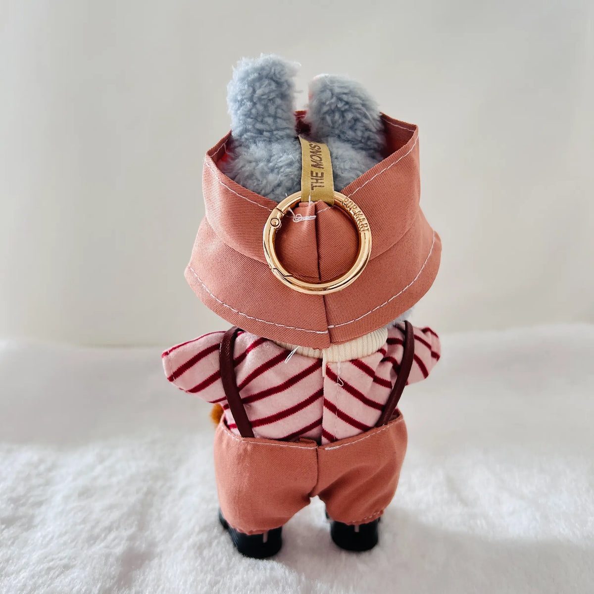 A back view of a Labubu doll wearing a dusty coral overalls, a red-and-white striped top, and black boots. 