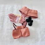 A doll outfit set laid flat on a white textured surface, including a peach satin-like top and skirt, a red-and-white striped bodysuit, a matching peach headband, and small black shoes.