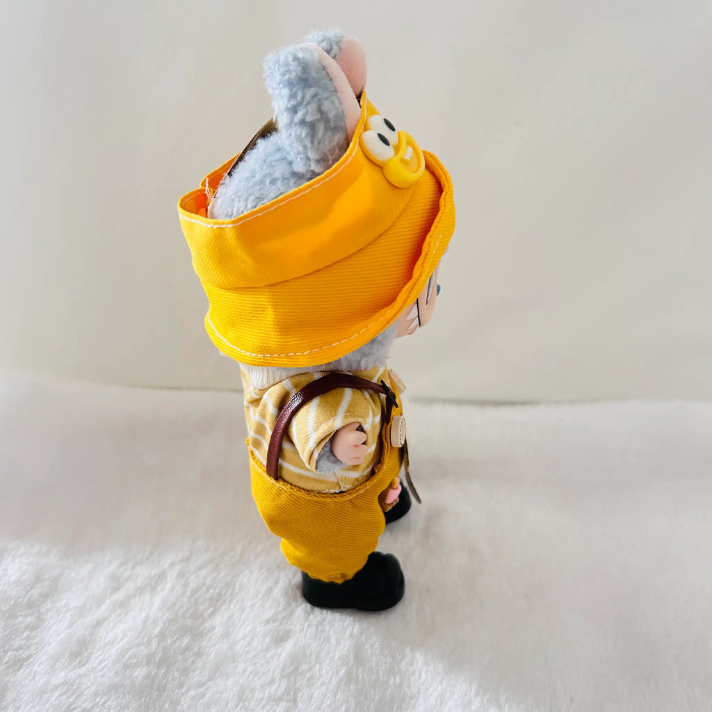 A Labubu doll wearing a bright yellow hooded outfit and black shoes, standing on a white textured surface against a plain light background.