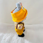 A Labubu doll wearing a bright yellow hooded outfit and black shoes, standing on a white textured surface against a plain light background.