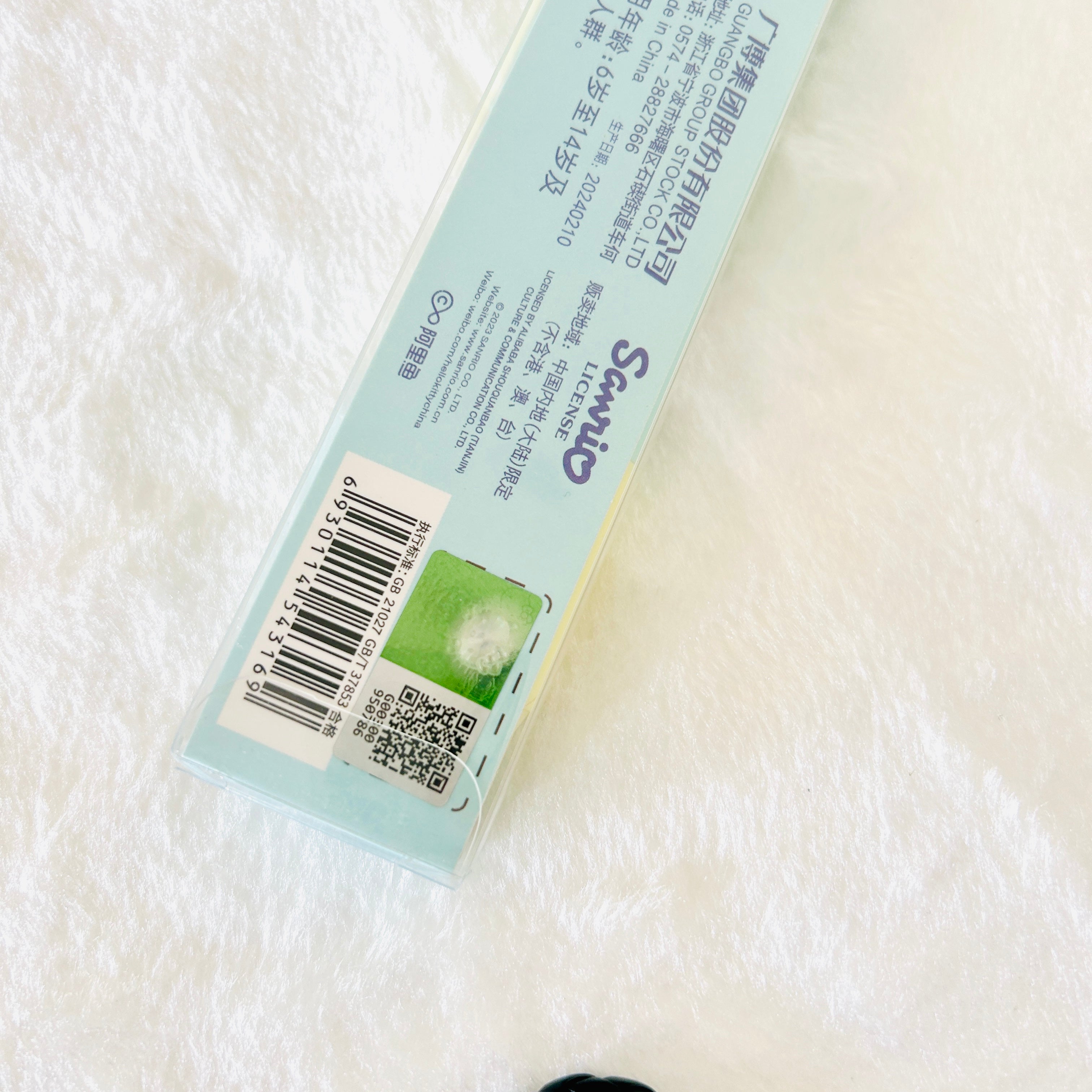 A close-up of a Scowl brand product box lying on a white textured fabric background. The box is light blue with black text, a barcode, a QR code, and a small green square graphic.