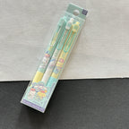 A packaged set of three pastel-colored gel pens with Sanrio character illustrations, resting on a split white and dark gray textured surface.