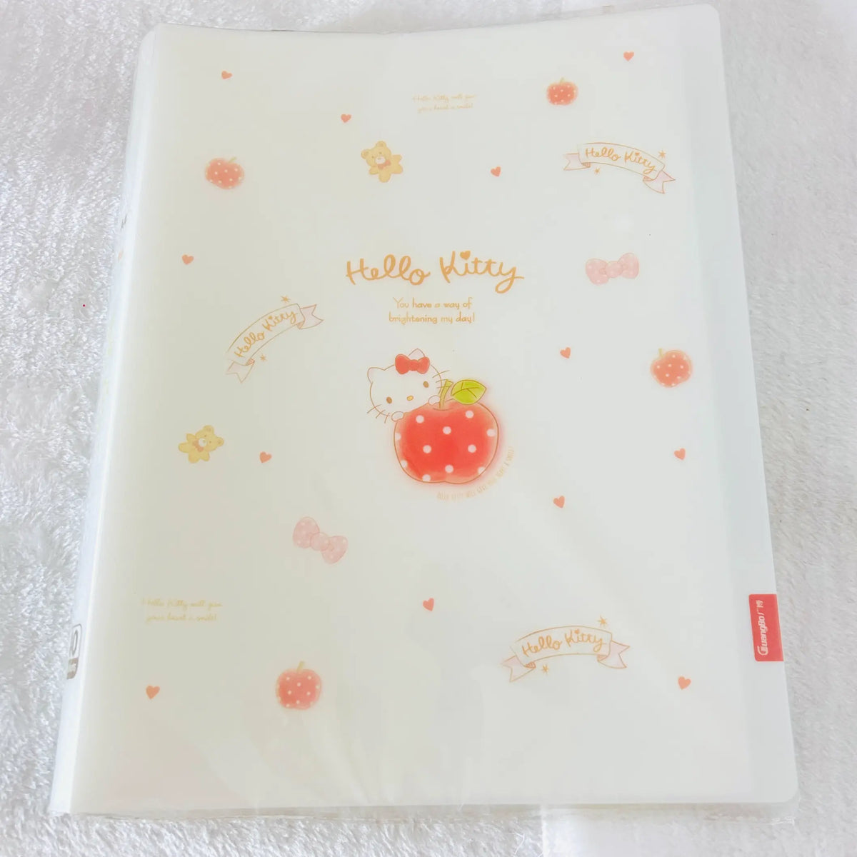 A translucent white plastic file folder featuring Hello Kitty designs, including a central apple illustration, 'Hello Kitty' text, small hearts, bows, and apples.