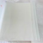 A close-up of a white planner or binder cover with a clear plastic sleeve attached on the left side, showing faint pink polka dots and a subtle logo on the cover.