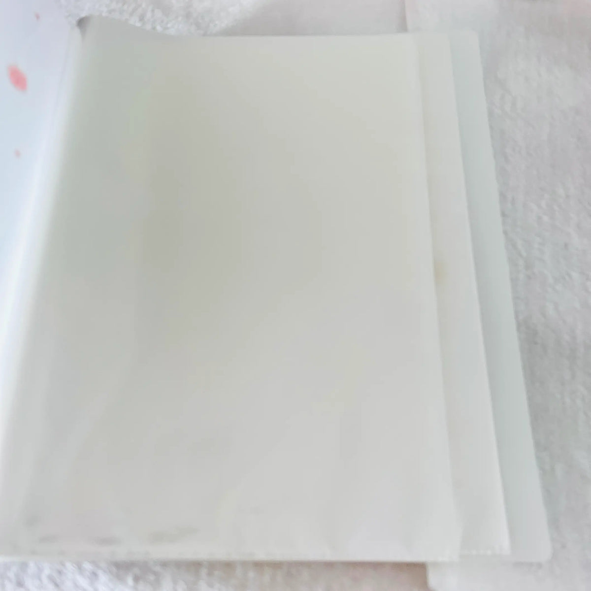 A close-up of a white planner or binder cover with a clear plastic sleeve attached on the left side, showing faint pink polka dots and a subtle logo on the cover.