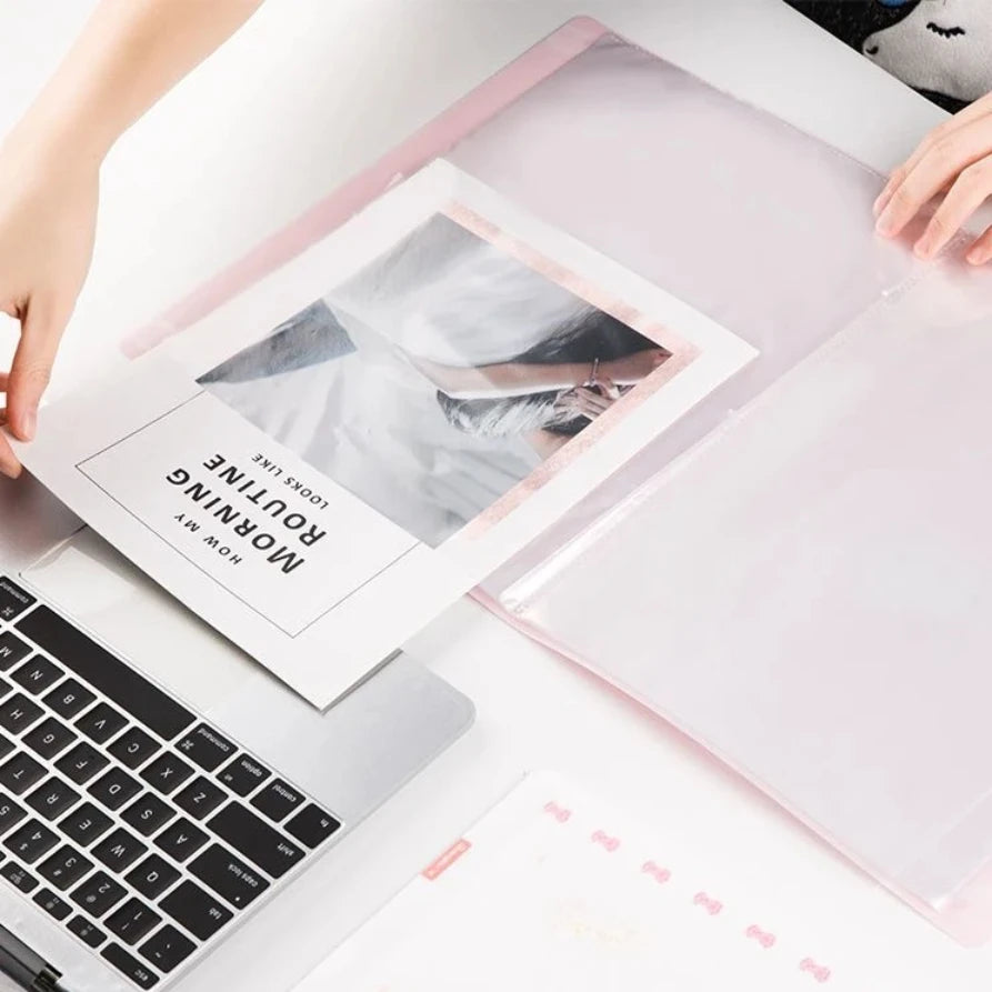 A translucent pink plastic photo organiser or binder sheet on a white desk, with hands holding it open and a printed card inserted.  