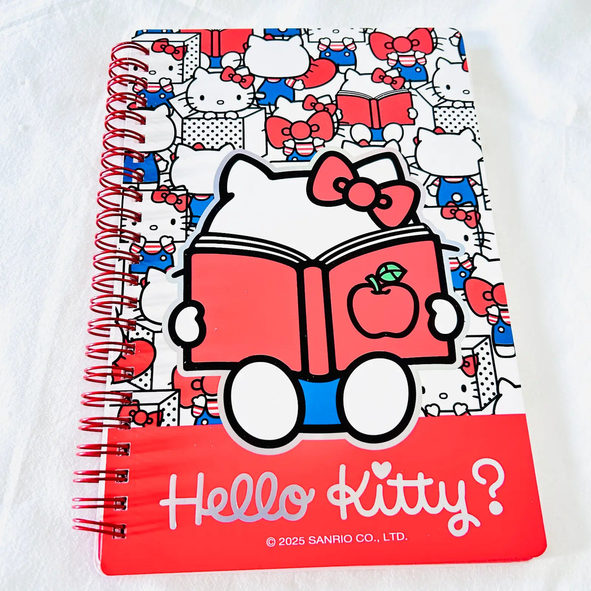 A spiral-bound notebook featuring Hello Kitty illustrations, with a large central character graphic reading 'Hello Kitty?' and a red bottom band with copyright text for Sanrio.