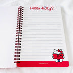 A spiral-bound Hello Kitty lined notebook on a white fabric background, with the red 'Hello Kitty?' title at the top and a small Hello Kitty illustration near the bottom right.