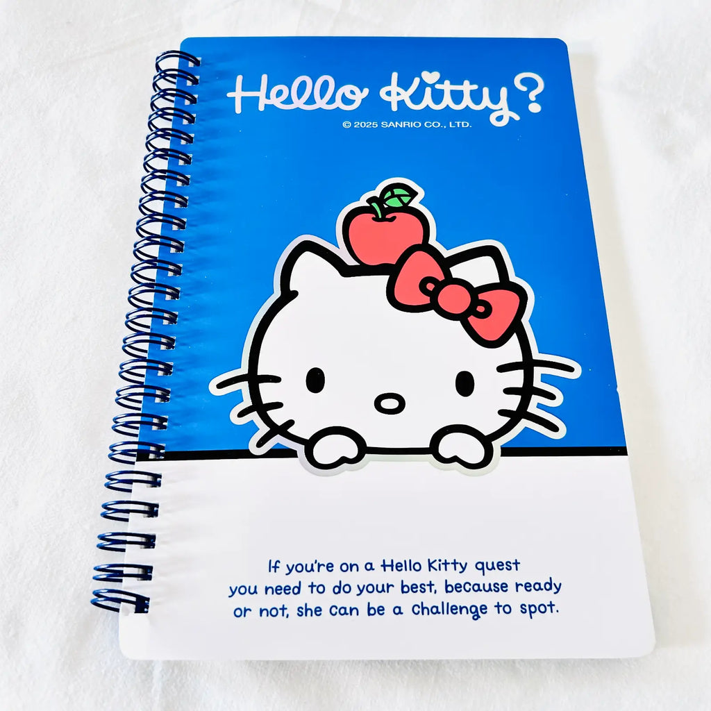 A spiral-bound notebook featuring Hello Kitty artwork on a blue and white cover, photographed on a white textured fabric background.
