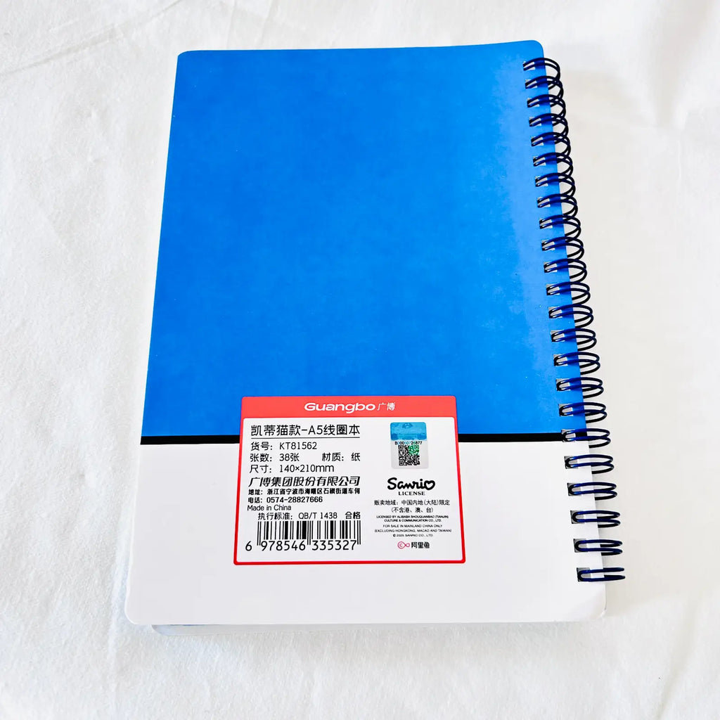 A blue spiral-bound notebook with a white cover and a red product label on a white fabric background. The brand 'duangbo' is visible on the label.