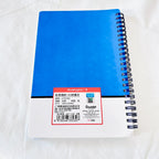 A blue spiral-bound notebook with a white cover and a red product label on a white fabric background. The brand 'duangbo' is visible on the label.