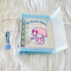 A Sanrio 'My Sweet Piano' ring binder notebook with a pink-haired character illustration, displayed on a white faux fur background alongside a blue beaded chain.